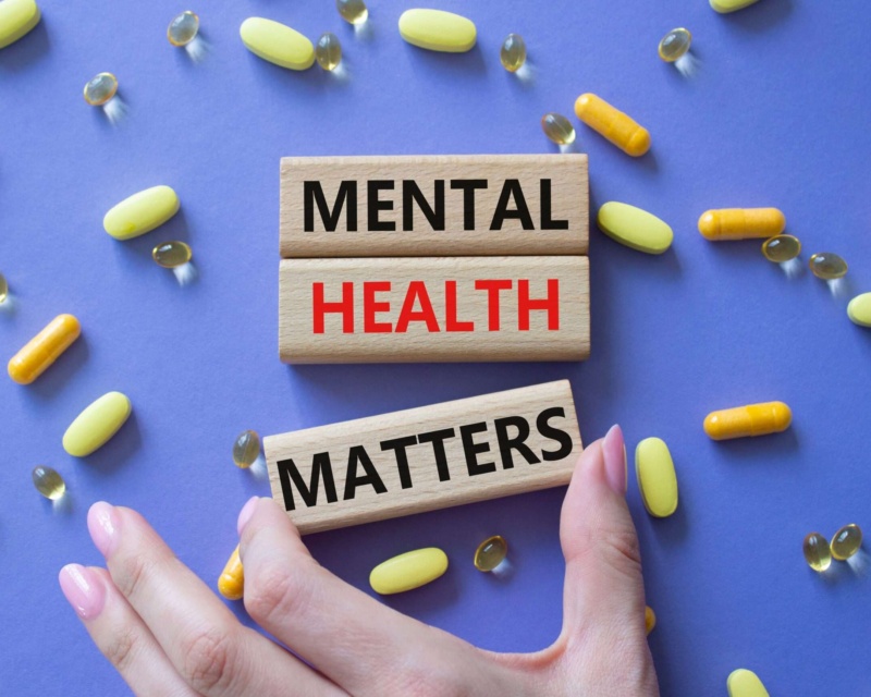 Wooden blocks spelling “Mental Health Matters” surrounded by yellow and orange capsules on a purple background.