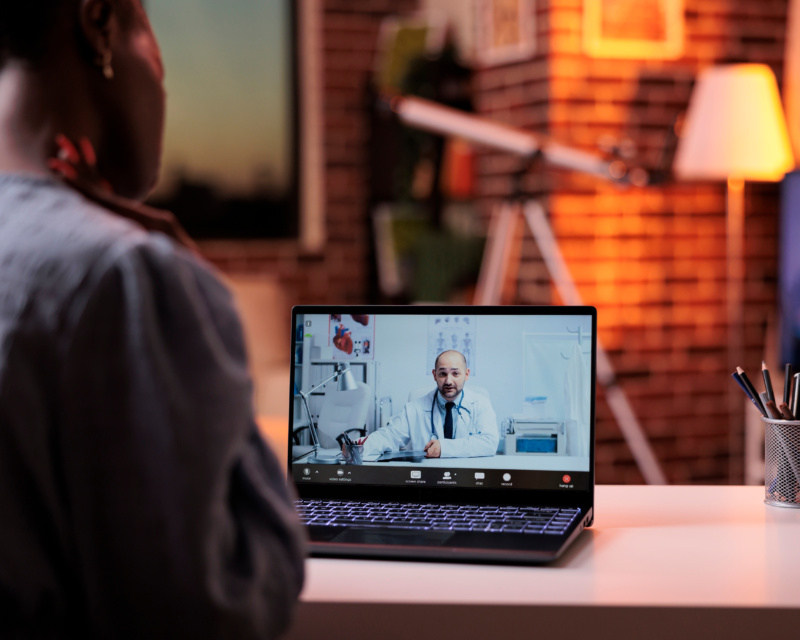 Patient attending an online telehealth consultation with a doctor on a laptop screen.