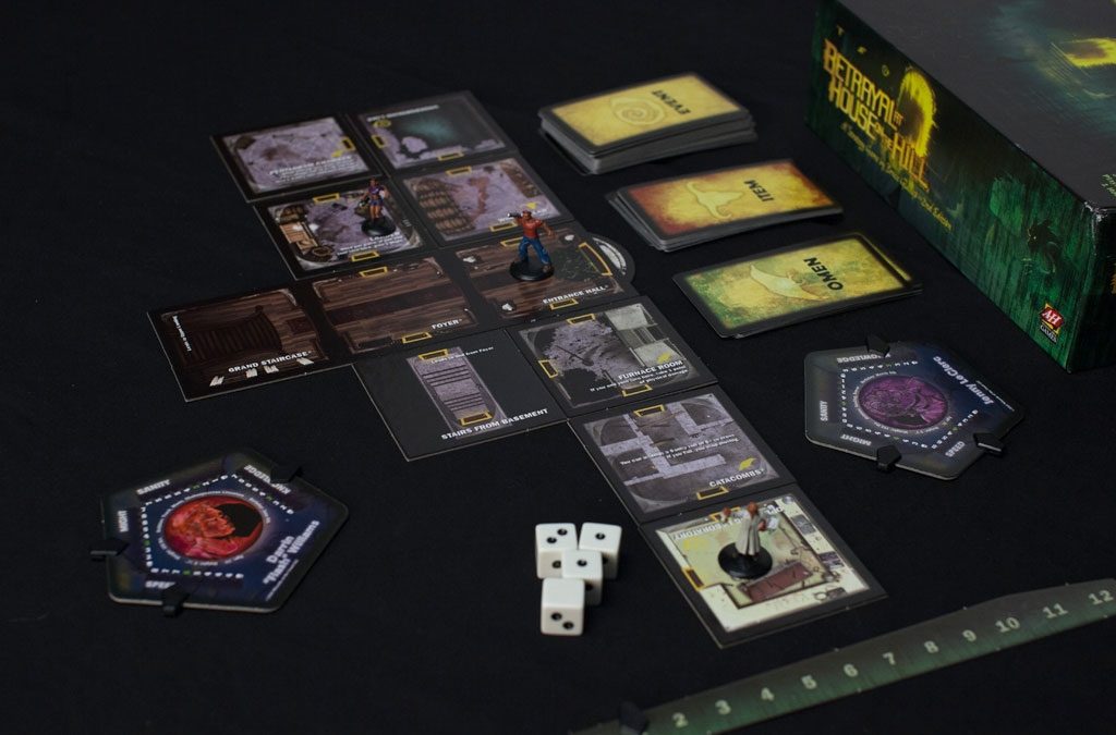Betrayal at the House on the Hill game pieces, including board, playing cards, dice, and character pieces. 2016 Brands We Love.
