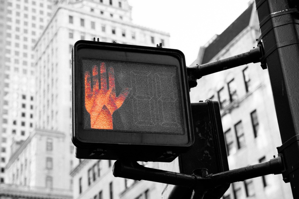 Stop signal in cityscape. Red illuminated hand on a city traffic signal indicating stop.