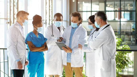 six healthcare professionals standing together looking at notes
