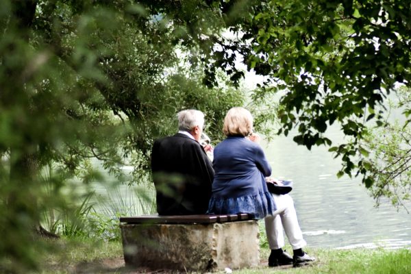 Senior couple sitting on a bench overlooking a lake while each is having a glass of wine. 